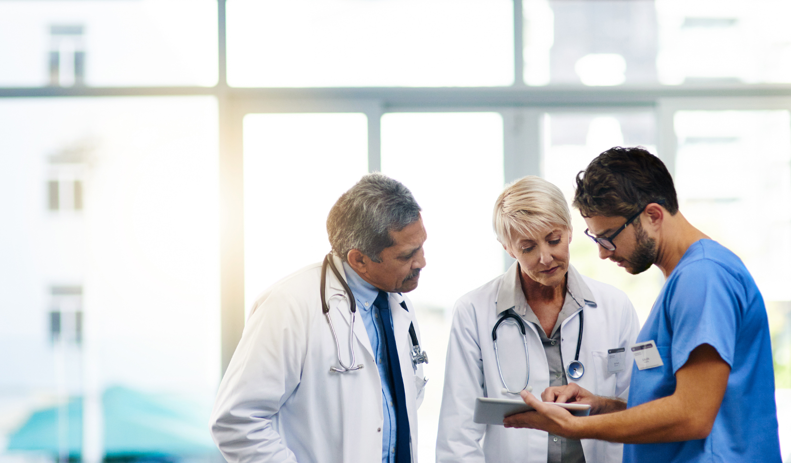 Three doctors, one younger and two older, look at an iPad. Credit: iStock/PeopleImages