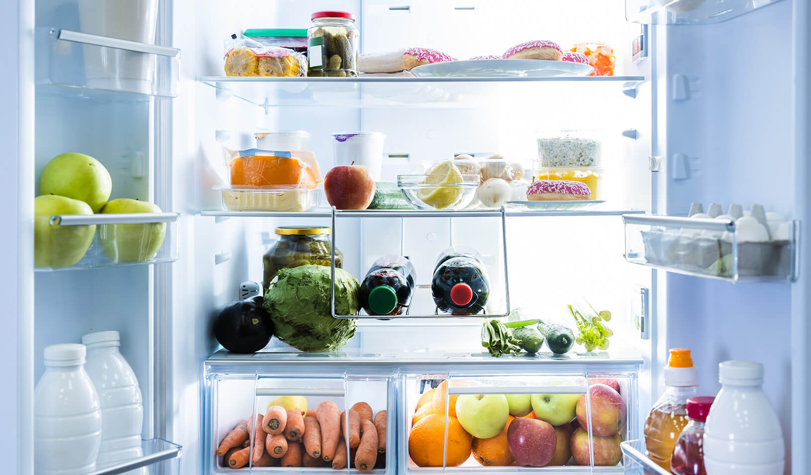 An open refrigerator that's clean and brightly lit, full of fruit, vegetables and junk food. | iStock/AndreyPopov.