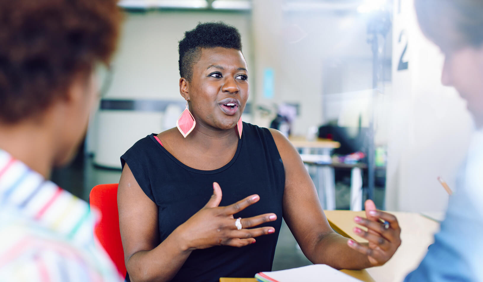 A Black woman sitting in a conference room with other woman, using her hands to gesture and looking happy. | Credit: iStock/julief514.