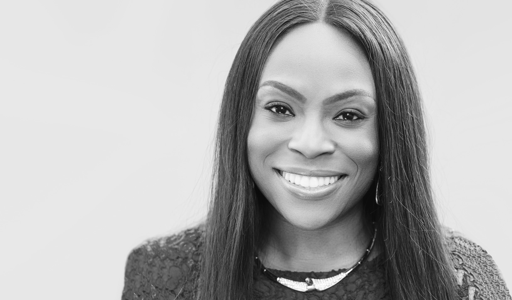 Black and white portrait of Dara Treseder smiling into the camera on a white background. Courtesy of Dara Treseder