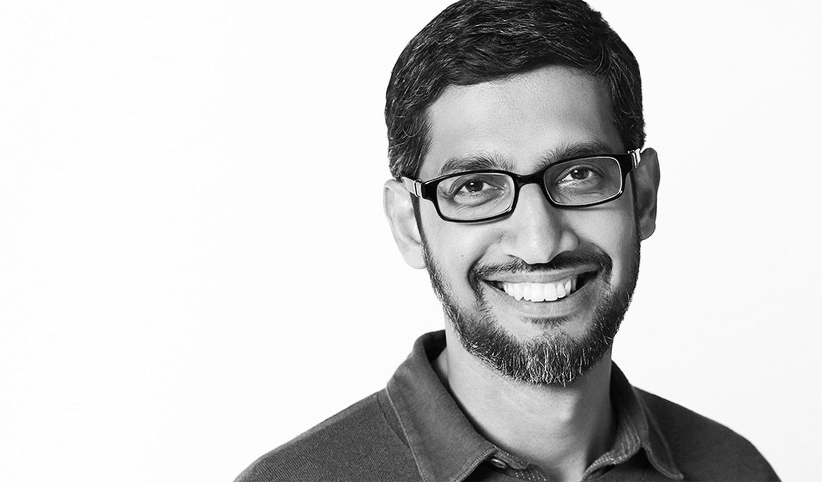 Black and white portrait of Sundar Pichai smiling at the camera in front of a white background. Courtesy of Sundar Pichai