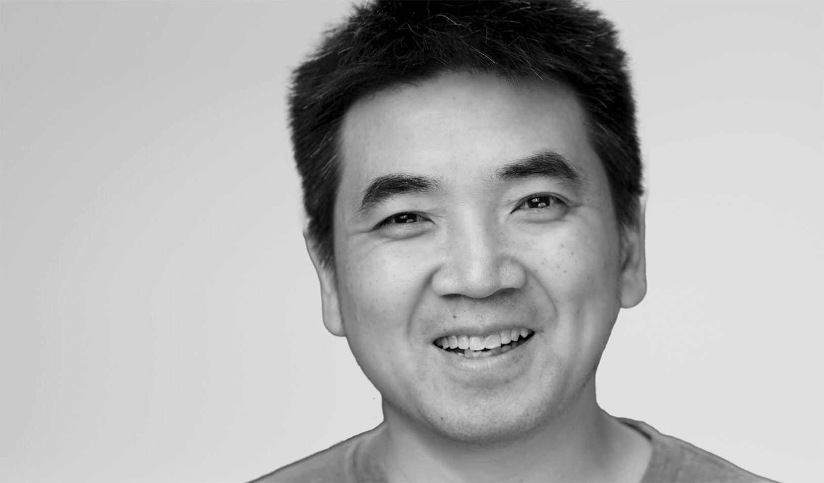 Black and white portrait of Eric Yuan smiling at the camera. Courtesy of Eric Yuan