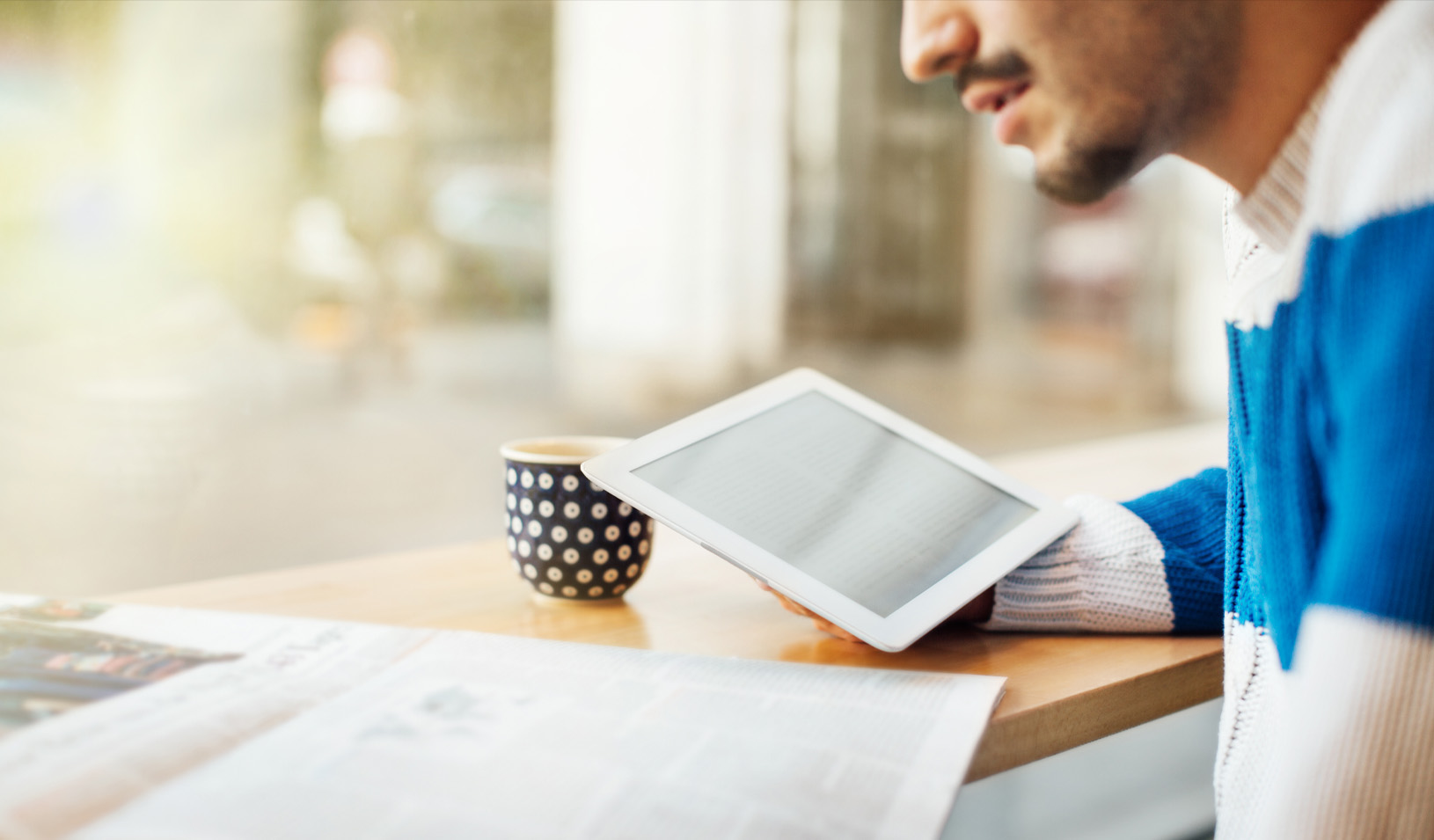 a man hunched over a table looking at a newspaper and an iPad. Credit: iStock/alvarez