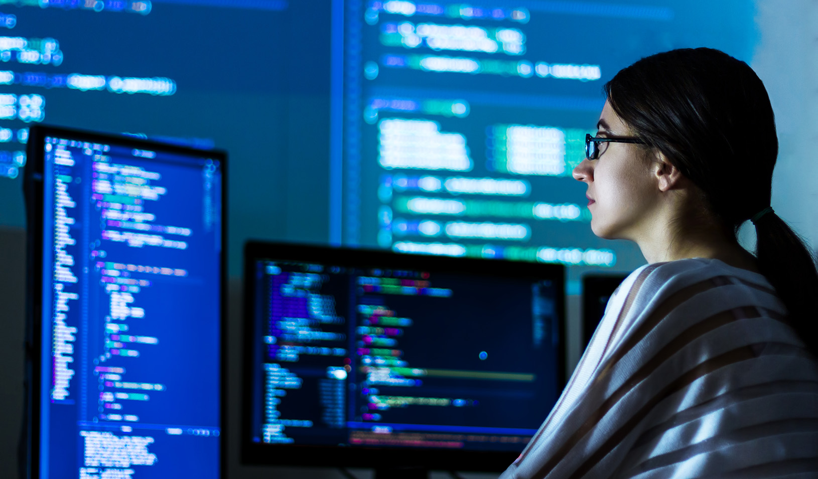 A woman wearing glasses looks at code on a computer screen.