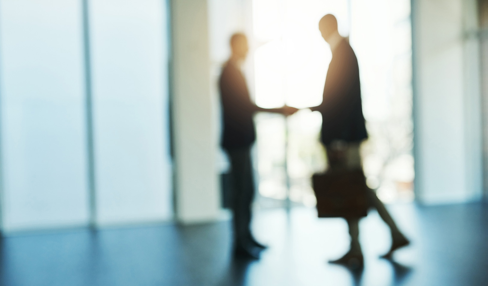 An out of focus image of two business people shaking hands in a corporate office. iStock/PeopleImages