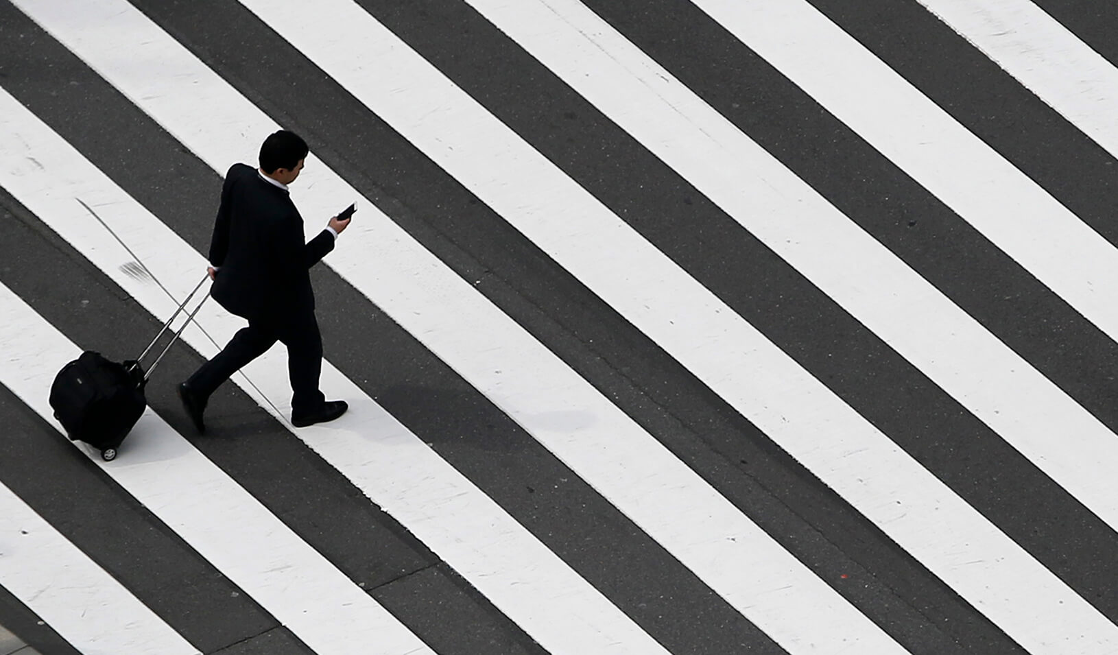 A businessman walks across the street, wheeling a bag. | Reuters/Yuya Shino