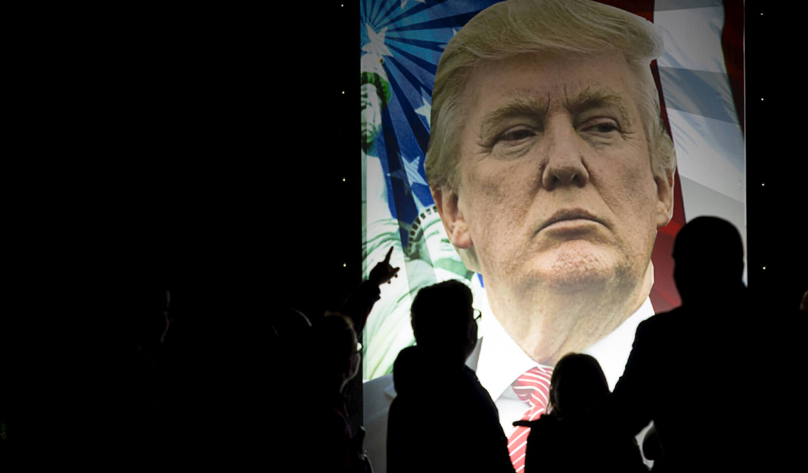 People silhouetted against an illuminated ad for Donald Trump. Credit: Reuters/Gretchen Ertl