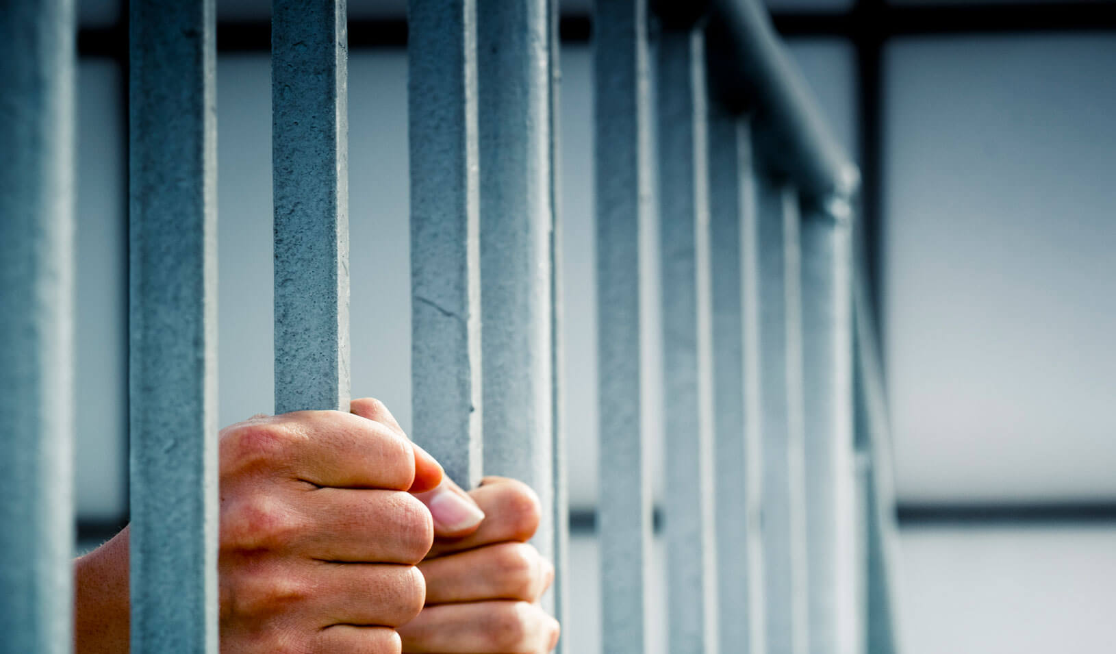 Hands grip the bars of a jail cell | iStock/chinaface