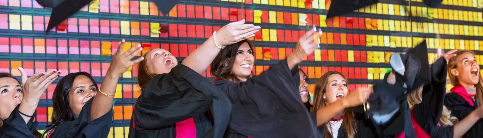 A line of women in graduation gowns throwing their caps in the air