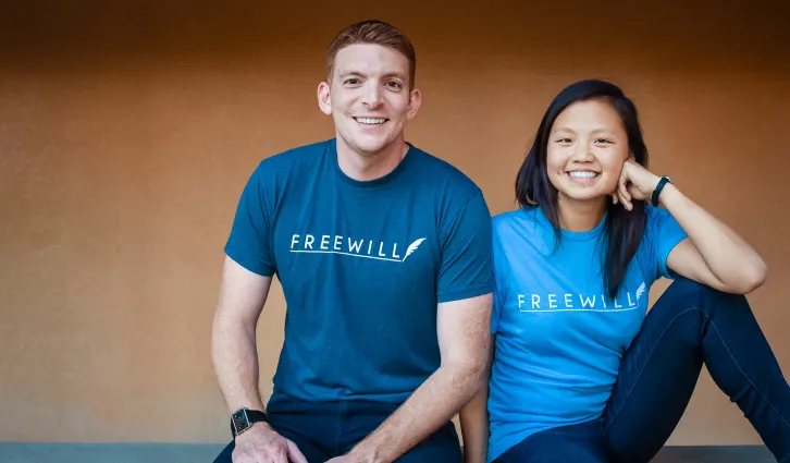 Portrait of Patrick Schmitt and Jenny Xia Spradling sitting next to each other outside, smiling at the camera.