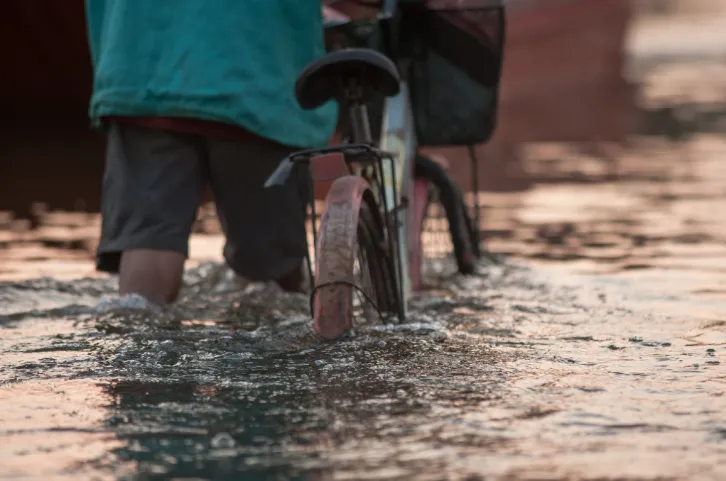 Image flooded water and person with bike walking through it