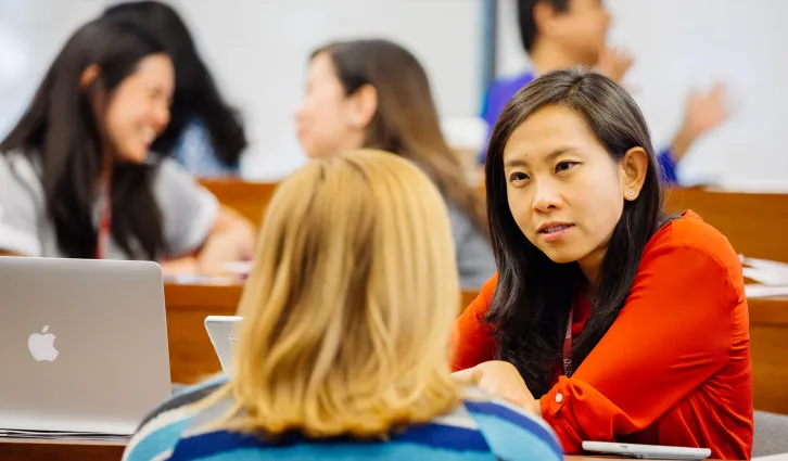 Two women talking in a classroom of other students. Credit: Elena Zhukova