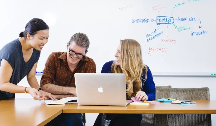 Three individuals brainstorming over a computer, laughing. Credit: Elena Zhukova